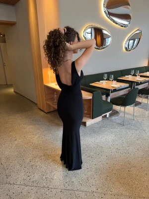Klänning med djuprygg - Flora maxi dress  - Elegant svart långklänning med djup v-ringning och öppen rygg. Klänningen har en figurnära passform och är tillverkad i ett mjukt, följsamt material som ger en snygg siluett. 