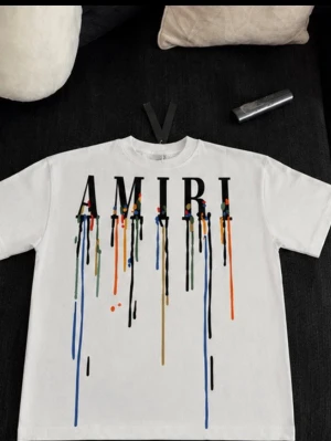 AMIRI t-shirt med färgstänk - Snygg vit t-shirt från AMIRI med stort tryck framtill där bokstäverna har färgstänk och droppar i blått, orange, grönt och svart. Klassisk passform och rund halsringning. Perfekt för dig som gillar streetwear och vill sticka ut. Helt ny aldrig andvänd med tags och allt 