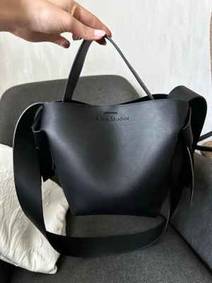 Svart handväska Acne Studios - Snygg svart handväska musubi mini Acne Studios. Skriv vid funderingar. Kvitto från förra säljaren finns, köpt på farfetch. Säljer då jag köpte likadan i mindre storlek. Priset är förhandlingsbart❣️använd cirka 3 gånger så inga större skador/slitningar. Dustbag följs med