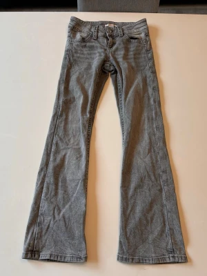 Grå bootcut jeans med broderade fickor - Säljer ett par grå bootcut jeans med snygga broderade detaljer på bakfickorna. Jeansen har klassisk femficksdesign och bälteshällor. Materialet är denim och färgen är en cool grå nyans som passar till det mesta.