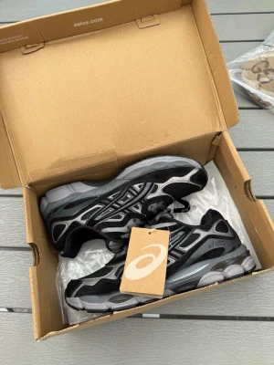 Svarta ASICS sneakers med silverdetaljer - Snygga svarta sneakers från ASICS med silver- och grå detaljer. Skorna har en sportig design med mesh och syntetmaterial, samt en rejäl sula för extra komfort. Perfekta för dig som gillar streetwear och vill ha en stilren look.