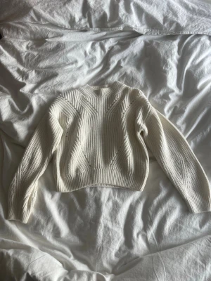Vit ribbstickad tröja med struktur - Säljer en vit ribbstickad tröja med snygga strukturdetaljer framtill. Tröjan har rund hals, långa ärmar och en croppad passform. Perfekt för dig som gillar stilrena och trendiga plagg i garderoben.