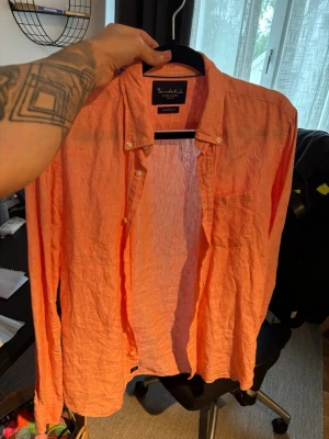 Orange linneskjorta från Benedict - Säljer en snygg orange skjorta från Brothers i luftigt linne. Skjortan har klassisk krage, lång ärm och knappar framtill. Perfekt för dig som vill ha en färgstark och bekväm skjorta till sommaren.