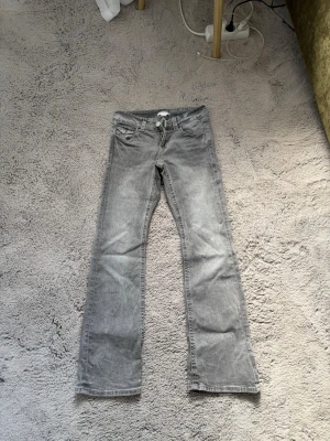 Grå bootcut jeans med fickdetaljer - Säljer ett par grå bootcut jeans med klassisk femficksdesign och snygga fickdetaljer bak. Jeansen har normal midja och är tillverkade i ett mjukt denimtyg. Perfekta för en avslappnad och trendig look.