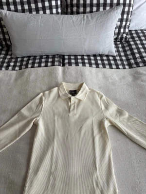 Vit ribbad henley från H&M - Säljer en vit långärmad henley från H&M i ribbad bomull. Skjortan har klassisk krage, knappar framtill och slim fit passform. Perfekt för dig som gillar stilrena och enkla plagg med en modern twist. Aldrig använd.