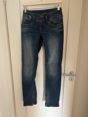 Blå jeans från LTB - Lågmidjade blå jeans från ITB med coola slitningar och dragkedjedetalj vid fickan. Jeansen har raka ben och dubbla knappar i midjan. Inte bootcut.