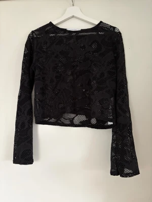 Svart spetsig långärmad topp Sisters Point prislapp kvar  - Trendig svart långärmad topp från Sisters Point i genombruten spets med coolt mönster. Croppad modell som ger en edgy vibe och passar perfekt till höga jeans eller kjol. Tillverkad i stretchig polyester och elastan för skön passform. Strl M oanvänd 