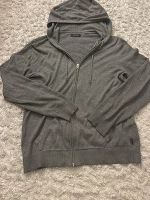 Grå zip merinowoll hoodie från Jack & Jones - Snygg grå hoodie med dragkedja från Jack & Jones . Tillverkad i mjukt material med ribbade muddar, två fickor fram och justerbar huva med snören. Perfekt för en chill och avslappnad stil.