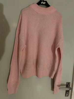 Ljusrosa stickad tröja med polokrage - Mysig ljusrosa stickad tröja med hög polokrage och avslappnad passform. Tröjan har långa ärmar och ribbade muddar vid ärmslut och nederkant. Perfekt för kalla dagar och enkel att matcha med jeans eller kjol.