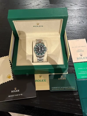 Rolex Submariner silver och svart - Säljer en stilren Rolex Submariner med svart urtavla och silverfärgad länk i rostfritt stål. Klockan har klassisk rund form och tydliga markeringar på vridringen. Kommer i originalbox med certifikat och tillbehör. Perfekt för dig som gillar exklusiva accessoarer.