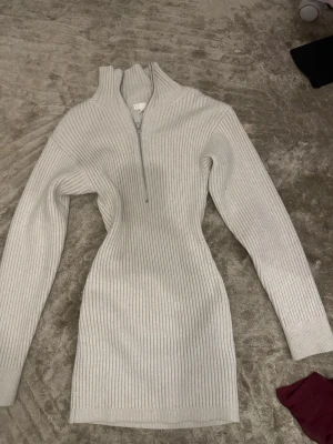 Ljusgrå stickad klänning med dragkedja - Säljer en ribbstickad ljusgrå klänning med lång ärm och halv dragkedja framtill. Klänningen har hög krage och figurnära passform, perfekt för lager-på-lager-stil. Materialet är mjukt och stretchigt för extra komfort. Har aldrig använt . Priset kan diskuteras 