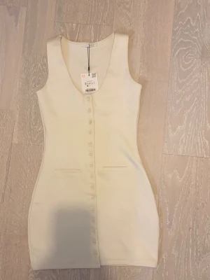 Zara krämvit klänning – NY med lapp  - Säljer en superfin krämvit figurnära klänning från Zara. Knappar framtill och små fickdetaljer. Oanvänd, prislapp kvar. Storlek S. ALDRIG ANVÄND !