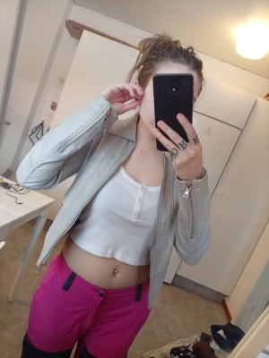 Ljusgrå skinnjacka med dragkedja - Säljer en ljusgrå skinnjacka med klassisk krage och dragkedja framtill. Jackan har raka ärmar med dragkedjor vid ärmsluten och stilrena sömdetaljer. Perfekt för dig som vill ha en snygg och enkel skinnjacka i garderoben. Lite skadad på kragen å även där man hänger upp den men funka utmärkt än