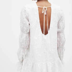 Vit broderad kortklänning med öppen rygg - Superfin vit kortklänning med broderade blommor, puffiga långärmar och öppen rygg med knytband. Klänningen har volang nertill och är gjord i ett lätt, luftigt material som känns perfekt för varmare dagar💕 Säljer då jag har två, så helt ny med prislappar kvar