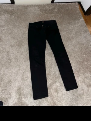 Svarta skinny jeans från Lee - Säljer ett par svarta skinny jeans från Lee med klassisk femficksmodell och dragkedjegylf. Jeansen har en smal passform och är tillverkade i ett stretchigt denimtyg som sitter snyggt. Perfekta till en avslappnad streetstyle-look.