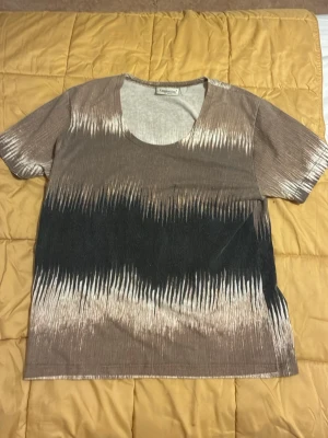 Missoni liknade Brun och svart t-shirt från Cappuccini - Snygg t-shirt från Cappuccini med unikt mönster i brunt och svart. T-shirten har korta ärmar och rund halsringning. Materialet känns mjukt och bekvämt, perfekt för en avslappnad stil.