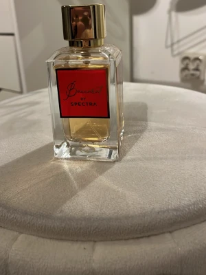 Baccarat by Spectra parfym - Elegant parfymflaska från Spectra med namnet Baccarat. Flaskan är rektangulär i genomskinligt glas med en röd etikett och guldfärgad kork. Innehållet är ljusgult och flaskan har en lyxig känsla.