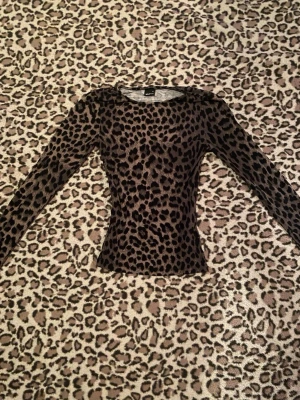 Leopardmönstrad topp  - Snygg långärmad topp från Gina Tricot i leopardmönster. Toppen har en tight passform och är tillverkad i ett mjukt, stretchigt material som känns bekvämt mot huden. Perfekt för dig som vill sticka ut med ett djuriskt print.