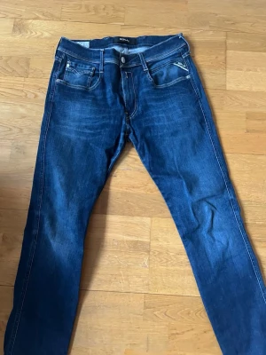 Mörkblå jeans från Replay Anbass - Säljer ett par mörkblå jeans från Replay, modell Anbass. Klassisk femficksdesign med raka ben och snygga slitningar. Jeansen har vita kontrastsömmar och är tillverkade i stretchigt denimtyg för extra komfort. Perfekta för en avslappnad och trendig look.