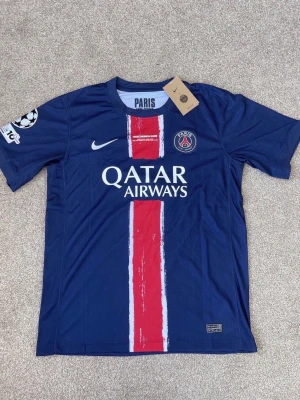 PSG matchtröja i mörkblått från Nike - Säljer en mörkblå Paris Saint-Germain matchtröja från Nike med klubbmärke och gul stjärna på bröstet. Tröjan har vita och röda detaljer samt tryck på insidan av kragen. Perfekt för dig som älskar fotboll och vill stötta PSG. Fraktar inom 24 timmar