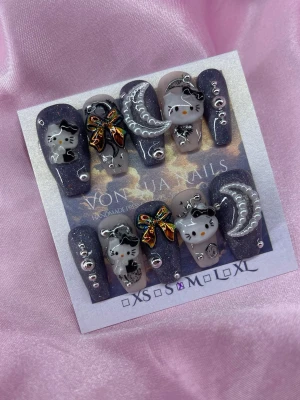 StarlitKitty (M); Medium Ballerina - Unika handgjorda press-on naglar med svart glitterbas, 3D dekorationer som söta HK, pärlmånar och färgglada rosetter. Naglarna har en mediumlång, ballerina form och är dekorerade med små silverpärlor. Perfekt för dig som vill ha en cool och lekfull look.M: 16 mm, 12 mm, 12,5 mm, 11,5 mm, 10 mm