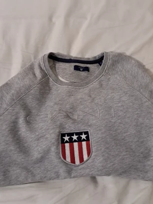 Gant sweatshirt - Snygg grå sweatshirt från GANT med broderad logga och sköld med stjärnor och ränder framtill. Klassisk rund halsringning och långa ärmar. Perfekt för en avslappnad och sportig stil.Start pros är 500 men den går och diskuteras vid intresse jätte bra tröja och snygg i samma tid 