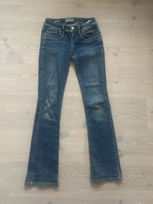 Blå bootcut jeans från LTB - Snygga blå bootcut jeans från LTBS med klassisk femficksmodell och slitna detaljer framtill. Jeansen har låg midja, dragkedja och knappstängning samt tydliga sömmar och patch med logga bak i midjan. Säljer pga dem är för små!