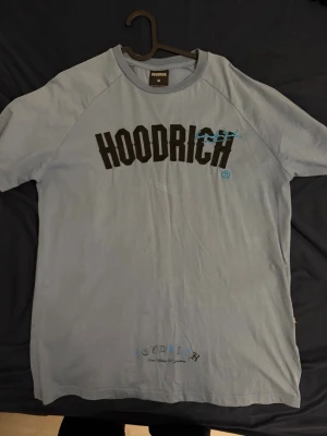 Ljusblå HOODRICH t-shirt - Säljer en ljusblå t-shirt från HOODRICH med stor svart logga och blå detaljer på bröstet. T-shirten har klassisk passform och korta ärmar. Tillverkad i mjuk bomull, perfekt för en avslappnad streetwear-look. Köpt för 800 i JD sports några månader sedan