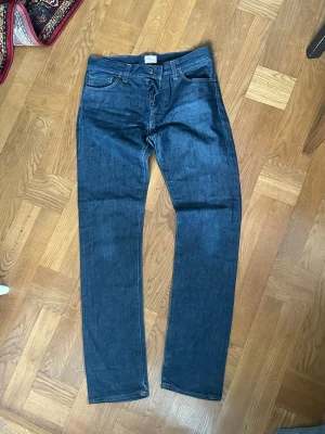 Mörkblå raka jeans från Denim Demon - Snygga mörkblå jeans från Denim Demon med rak passform och klassisk femficksdesign. Jeansen har synliga kontrastsömmar och knäppning med knappar framtill. Perfekta för dig som gillar en stilren och tidlös look.