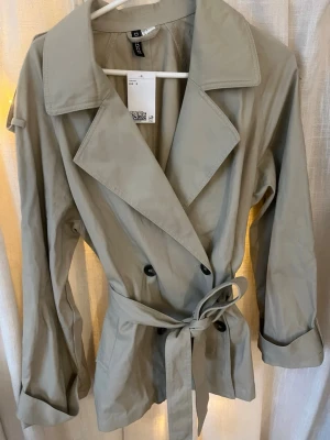Snygg trenchcoat  - Helt ny, trendig beige trenchcoat med dubbelknäppning från H&M. Storlek S