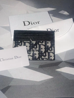 Dior svartvit korthållare - Snygg svartvit korthållare från Dior med det klassiska monogrammönstret. Tillverkad i canvas och läderdetaljer, perfekt för att hålla ordning på dina kort. Kommer med originalförpackning och dustbag.