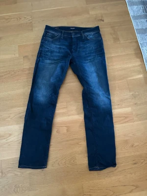 Mörkblå jeans från Jack & Jones - Snygga mörkblå jeans från Jack & Jones med klassisk femficksmodell och lätt slitna detaljer framtill. Jeansen har normal midja, raka ben och är tillverkade i denim med stretch för extra komfort. Perfekta för en avslappnad och trendig look.