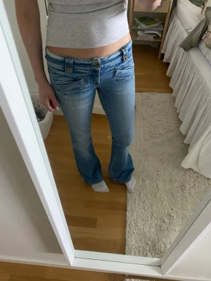 Ljusblå bootcut jeans med låg midja - Säljer ljusblå jeans med en design på fickorna där fram. Jättefina, köpt second hand. Inga defekter 💞