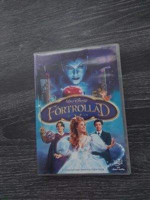 Disney DVD Förtrollad - Säljer en DVD med filmen Förtrollad från Walt Disney. Omslaget är färgglatt med blå och lila toner, och motivet visar karaktärer från filmen samt en stor röd äpple. Perfekt för dig som gillar magiska äventyr och musikal.