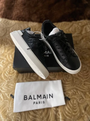 Svarta  sneakers i läder - Stilrena svarta sneakers  i slätt läder med vit sula och präglad logga på sidan. Klassisk låg modell med svarta skosnöre på plösen. Snygg kontrast mellan svart ovandel och vit yttersula.