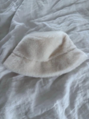 Vit fluffig bucket hat - Säljer en supermjuk och fluffig bucket hat i krämvit färg. Hatten har en klassisk form med bred brätte och är gjord i fuskpäls som ger en riktigt cozy vibe. Perfekt accessoar för att lyfta din outfit och hålla dig varm under kyliga dagar och skydda dig från solen under varma🌅❄️🤍