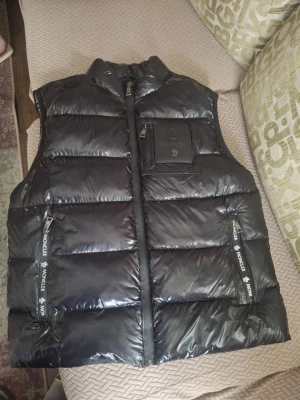 Moncler maya dunväst - Snygg svart tjock ÄKTA dunväst från Moncler med glansig finish och stora quiltade paneler. Västen har en hög krage, dragkedja framtill och en bröstficka med Moncler-logga i svart läder. Scanningsbar, aldrig använd. Storlek 5 som motsvarar L/XL