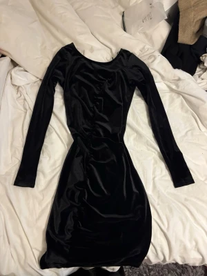 Svart sammetsklänning från Lindex - Snygg svart sammetsklänning från Lindex i kort modell med lång ärm och rundad halsringning. Klänningen har en figurnära passform och känns lyxig tack vare det mjuka sammetstyget. Perfekt för dig som vill sticka ut med en klassisk look.