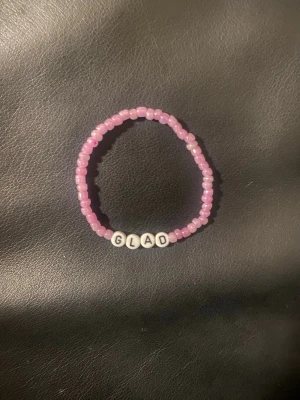Rosa pärlarmband med text - Ett sött armband med rosa pärlor och vita bokstavspärlor som stavar ordet 'GLAD'. Armbandet är elastiskt och passar de flesta handleder. Perfekt accessoar för att sprida positiv energi.