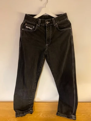 Svarta Kickers jeans med kontrastsömmar S/M - Säljer ett par svarta jeans från Kickers med vita kontrastsömmar och broderad logga på bakfickan. Klassisk femficksmodell med rak passform och knappgylf. Perfekta för dig som gillar streetwear och vill sticka ut lite extra. Passar storlek S/M, baggy/oversizemodell. Ca 36 cm mätt tvärs över midjan. 