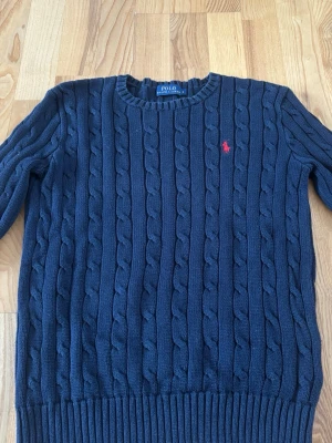 Stickad tröja från Ralph lauren - Kabelstickad tröja från Polo Ralph Lauren med rund halsringning och röd broderad logga på bröstet. Tröjan är begagnad.