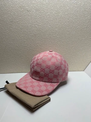 Rosa keps med GG-mönster - Säljer en rosa keps med det klassiska GG-monogrammet i en tonad rosa färg. Kepsen har böjd skärm, justerbart band bak i rosa läder och är tillverkad i canvasmaterial. Perfekt accessoar för dig som vill sticka ut med en lyxig touch.