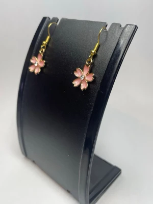 Rosa blomformade örhängen med strassdetalj - Söta örhängen i form av rosa blommor med guldfärgade krokar. Varje blomma har fem kronblad och en liten pärlliknande detalj i mitten som ger extra bling. Perfekta för dig som gillar gulliga accessoarer med en feminin touch.