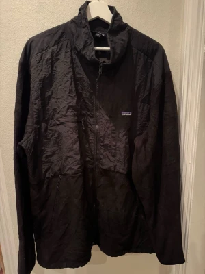Patagonia Hybrid jacka svart stl XL herr - Patagonia Hybrid i svart — nylonpaneler fram kombinerat med stretchig fleecebaksida. Heldragkedja, teknisk passform för friluftsliv. Mycket gott skick.