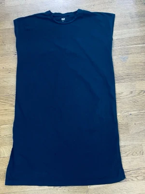 Svart ärmlös bomullsklänning - En enkel svart klänning i rak modell med ärmlös design och rund halsringning. Tillverkad i mjuk bomull, perfekt för en avslappnad och stilren look. Klänningen har en klassisk och minimalistisk stil utan mönster eller extra detaljer.