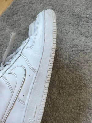 Vita Nike Air Force 1 sneakers - Klassiska vita Nike Air Force 1 sneakers med låg profil och tydlig swoosh-logga på sidan. Skorna har en tjock, mönstrad sula och är tillverkade i läder med vita snören. Perfekta för en clean och stilren look. Säljes på grund av att de är för små🤍