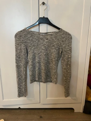 Gråmelerad stickad tröja med öppen rygg - Säljer en gråmelerad stickad tröja med lång ärm och snygg snörningsdetalj i ryggen. Tröjan har en kroppsnära passform och bredare ringning fram. Perfekt för dig som gillar en enkel men trendig look. Pris kan diskuteras. Köparen står för frakt.