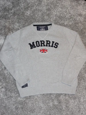 Grå stickad tröja från Morris - Står S men passar även M utan problem.Tröjan har inga defekter. Hör av dig vid frågor🌟Snygg grå stickad tröja från Morris med svart broderad logotyp och brittisk flagga på bröstet. Tröjan har rund halsringning, ribbstickade muddar och är perfekt för en stilren look. 