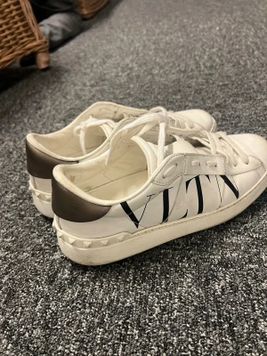Vita Valentino Garavani sneakers - Snygga vita sneakers från Valentino Garavani med svart VLTN-logga på sidan och nitar runt hälen. Lite använda men har mycket kvar att ge, hör av er vid fler frågor💕💕