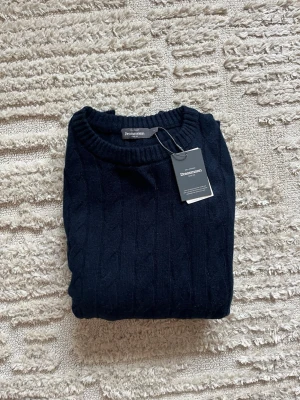 Mörkblå kabelstickad tröja - Kabelstickad mörkblå tröja från Dressmann. Den är i sprillans nytt skick och är aldrig använd med lappen kvar. Passformen är L och väldigt len ull. Skriv i DM om du har frågor 🥂